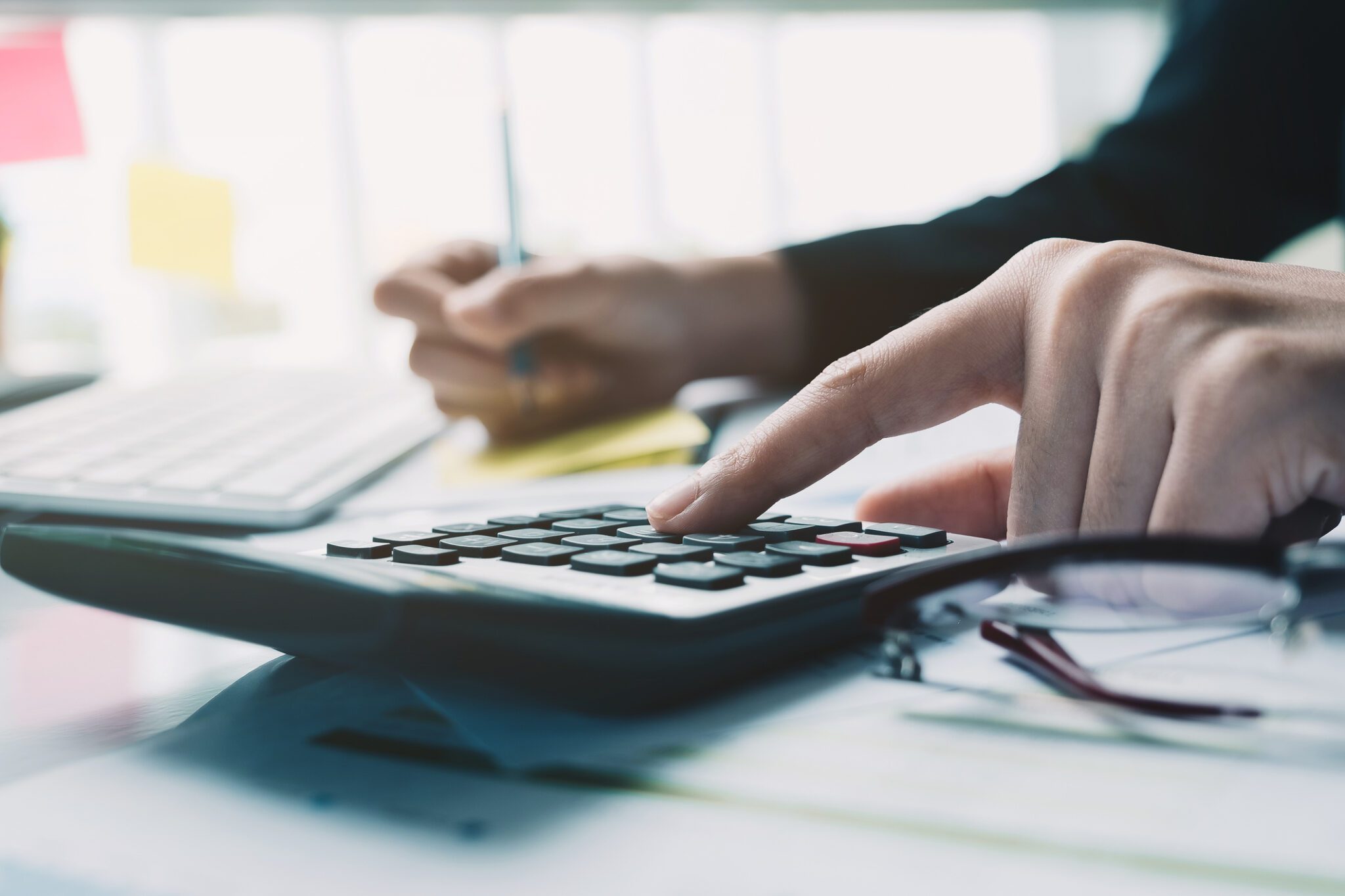 Businessman using a calculator and taking notes to define key bid metrics for tendering