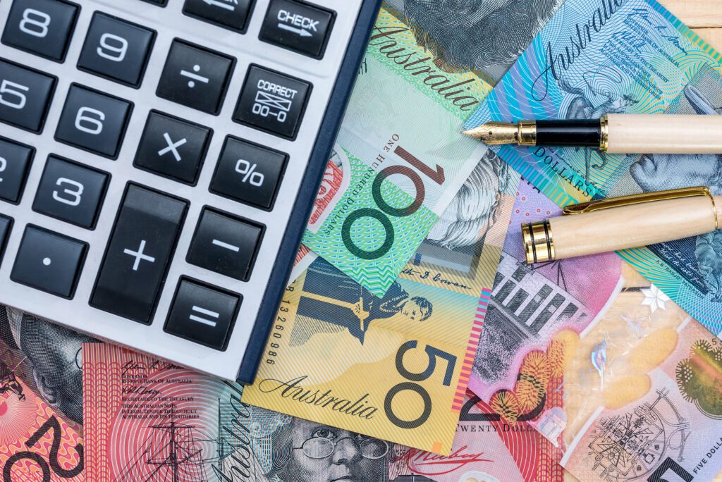 A calculator and pen with money (Australian dollars) on a table - representing calculated tendering investments.